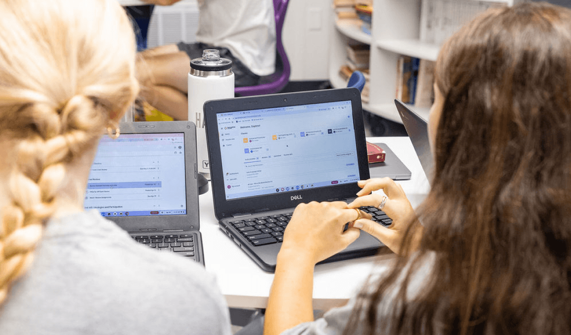 Two students working side by side on laptops in class