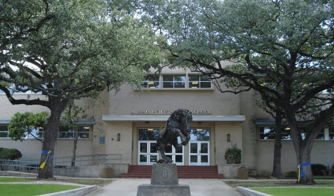 The Alamo Heights school building and mule statue framed by live oaks